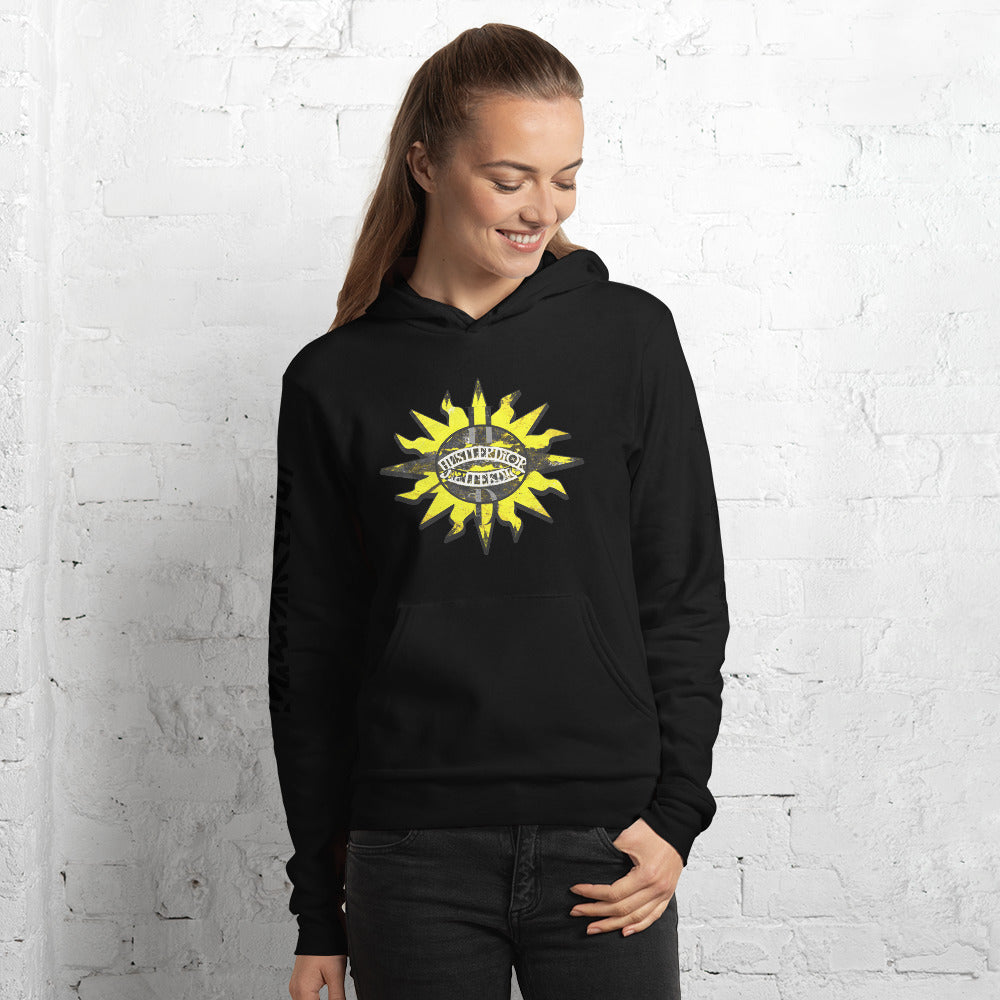 A woman wearing a black hoodie with a yellow sun graphic stands in front of a white brick wall.