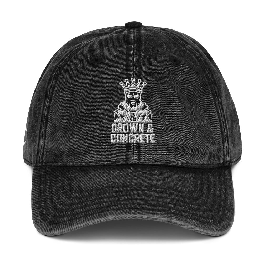 Black denim baseball cap with a white graphic featuring a crowned figure and the text "CROWN & CONCRETE".
